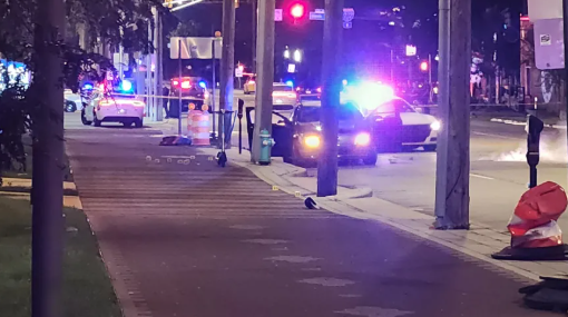Night street scene with emergency vehicles, flashing lights, and a red traffic cone on the sidewalk.