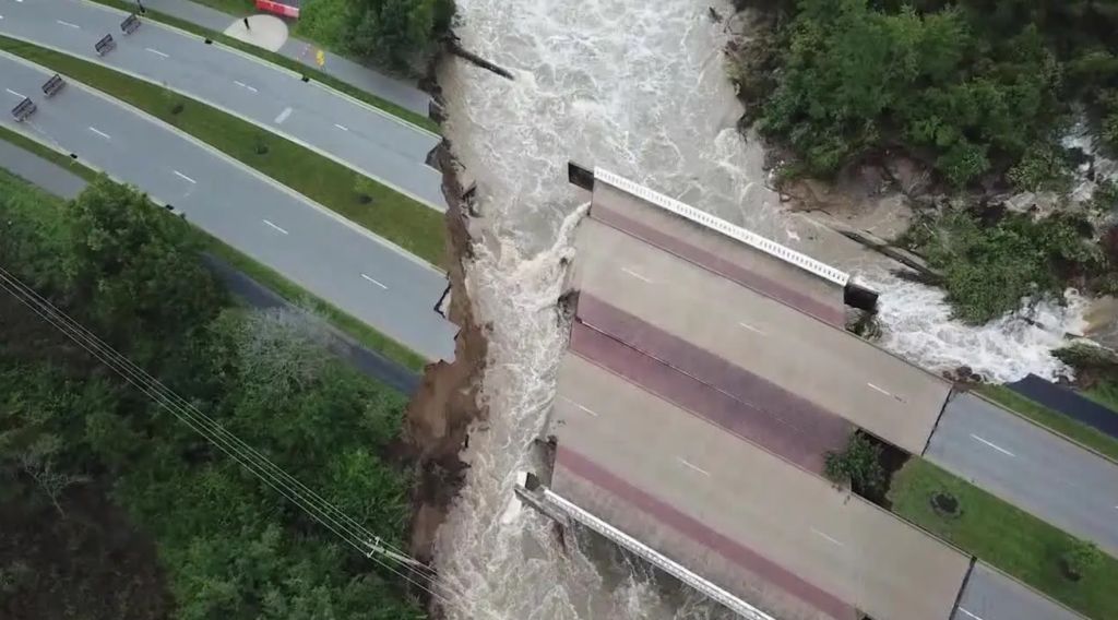 A rushing river flows through a steep ravine, with a damaged bridge or structure partially collapsed into the water.