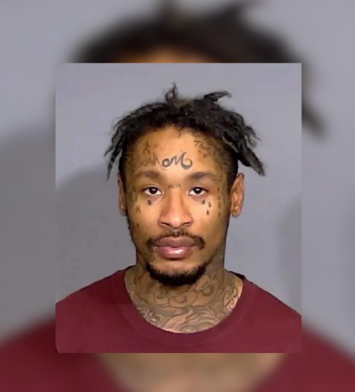 Headshot of a man with dreadlocks, facial tattoos, and a red shirt.