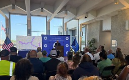 A crowd of people gathered in a room with American flags and a large display board.