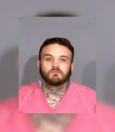 Headshot of a man with a beard and tattoos wearing a pink shirt.