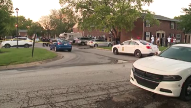 A street scene with several police cars and officers on the sidewalk, surrounded by trees and buildings.