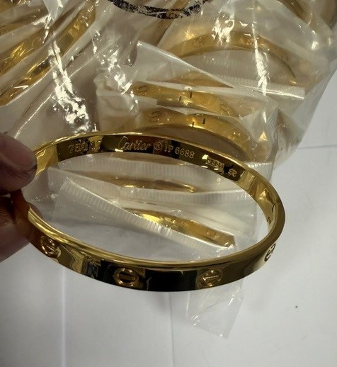 A gold-colored bangle bracelet with the engraved text "Cartier 18k 6888".