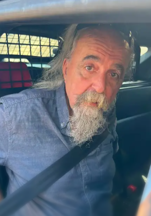 Older man with long gray beard wearing a blue shirt and sitting in a vehicle.