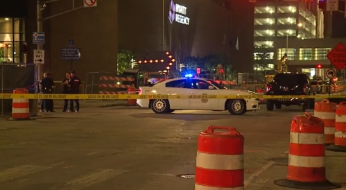 A police car with flashing lights parked on a city street at night, surrounded by construction cones and barricades.