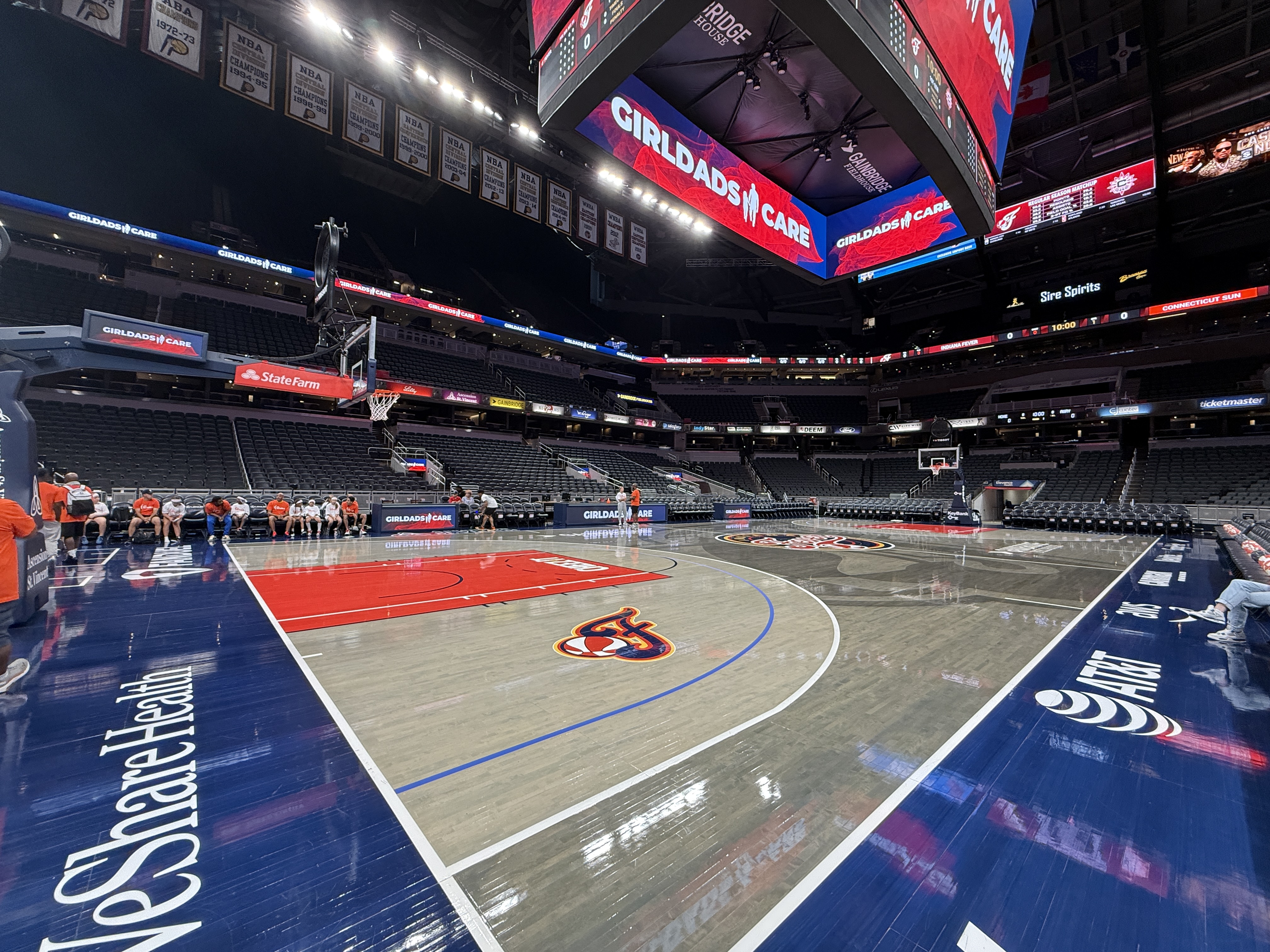 An indoor basketball arena with a large court, scoreboard, and signage for "Girdads in Care" and "State Farm".