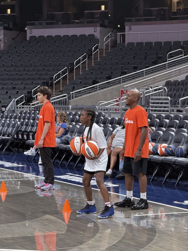 Basketball players in orange shirts standing on a basketball court in an empty arena.